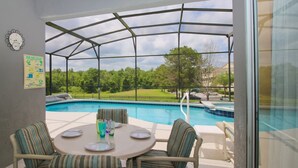 Eine überdachte Terrasse mit Blick auf den Pool, ausgestattet mit einem Tisch, Stühlen und einer Wanduhr.