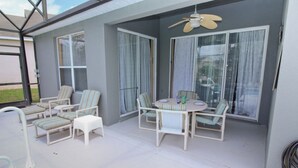 A covered patio area with a round table and chairs, a ceiling fan, and large windows with curtains. - Luxury Villa  Private Pool And Great Game Room (Kissimmee)