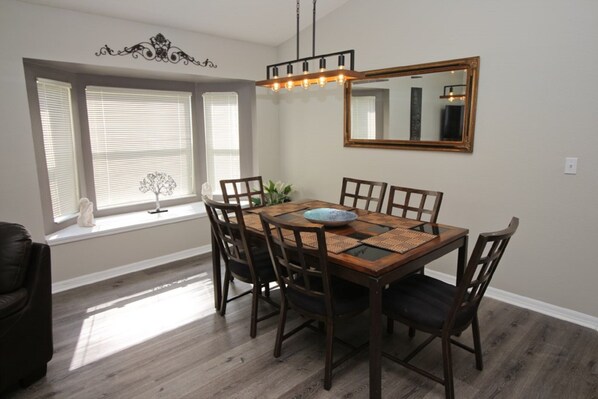 Un coin repas comprenant une table en bois, six chaises, un miroir décoratif et un luminaire suspendu.