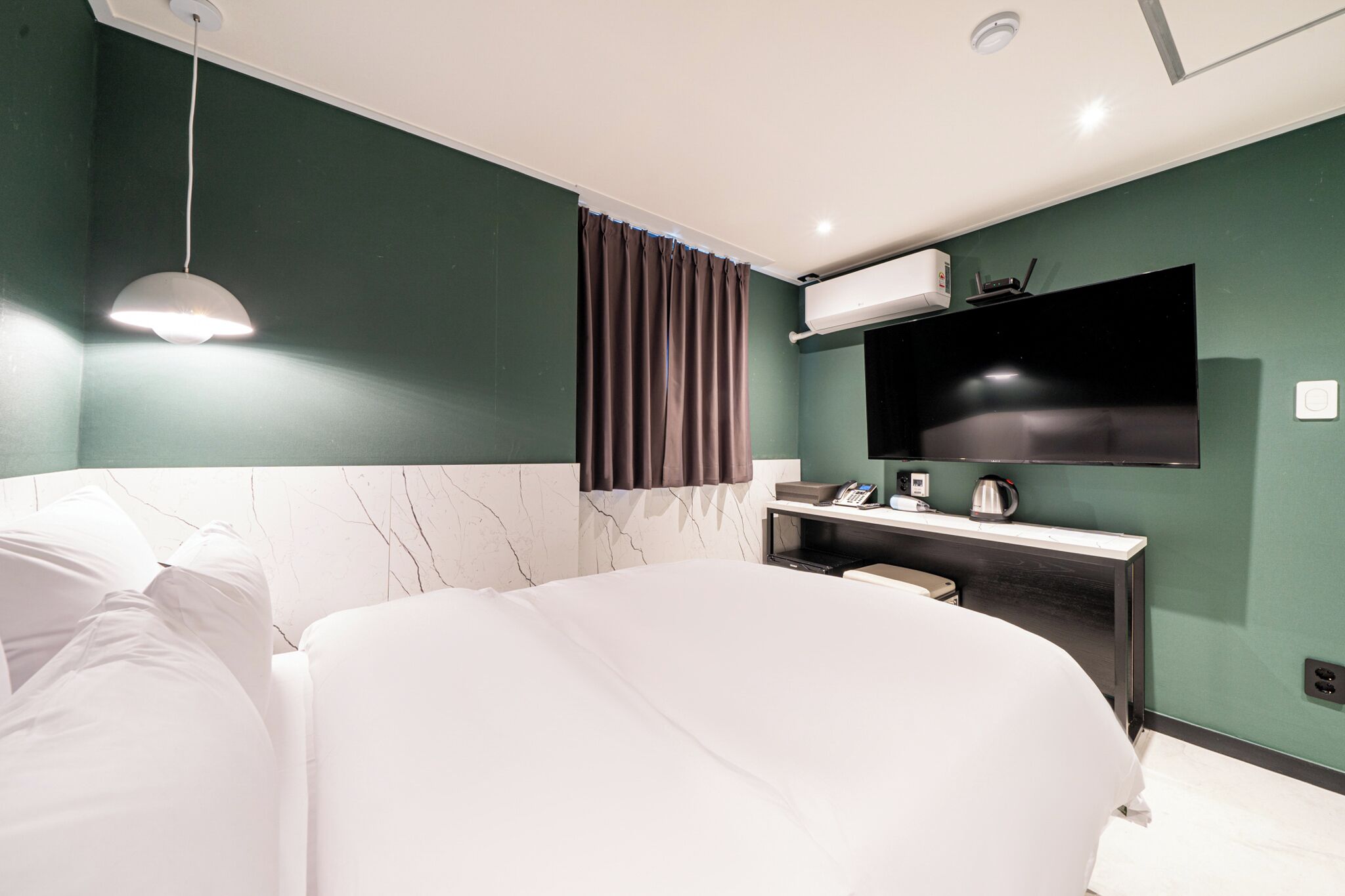 Une chambre d’hôtel moderne dotée d’un grand lit, d’un téléviseur à écran plat fixé au mur, d’une table de chevet avec une lampe et d’une fenêtre avec des rideaux.