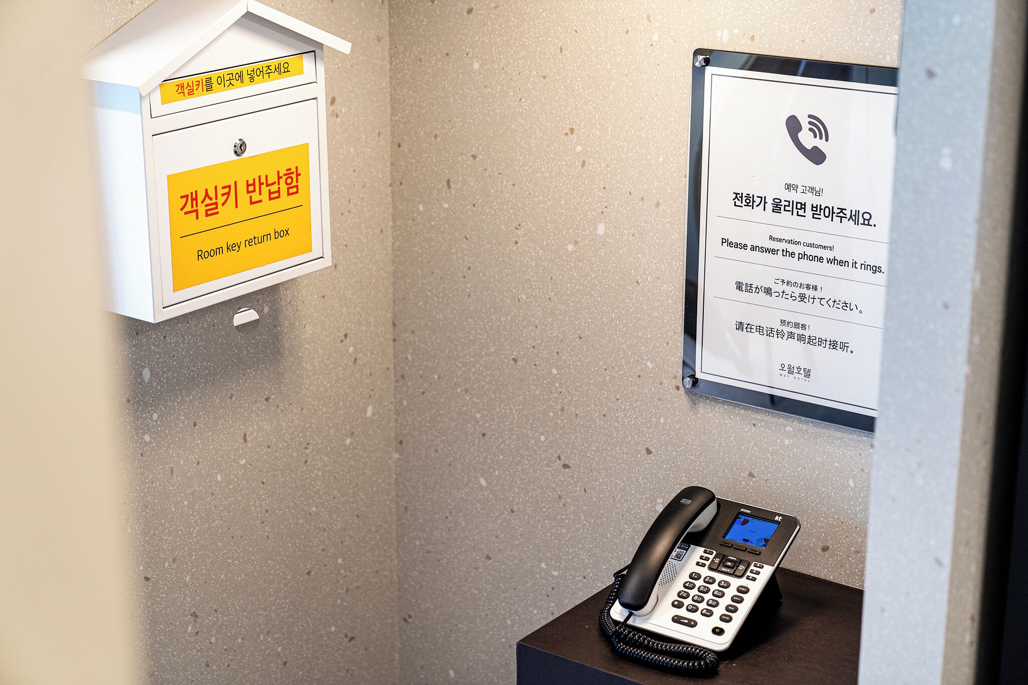 A room with a phone, a wall-mounted box with a yellow sign, and a message board with instructions in Korean.