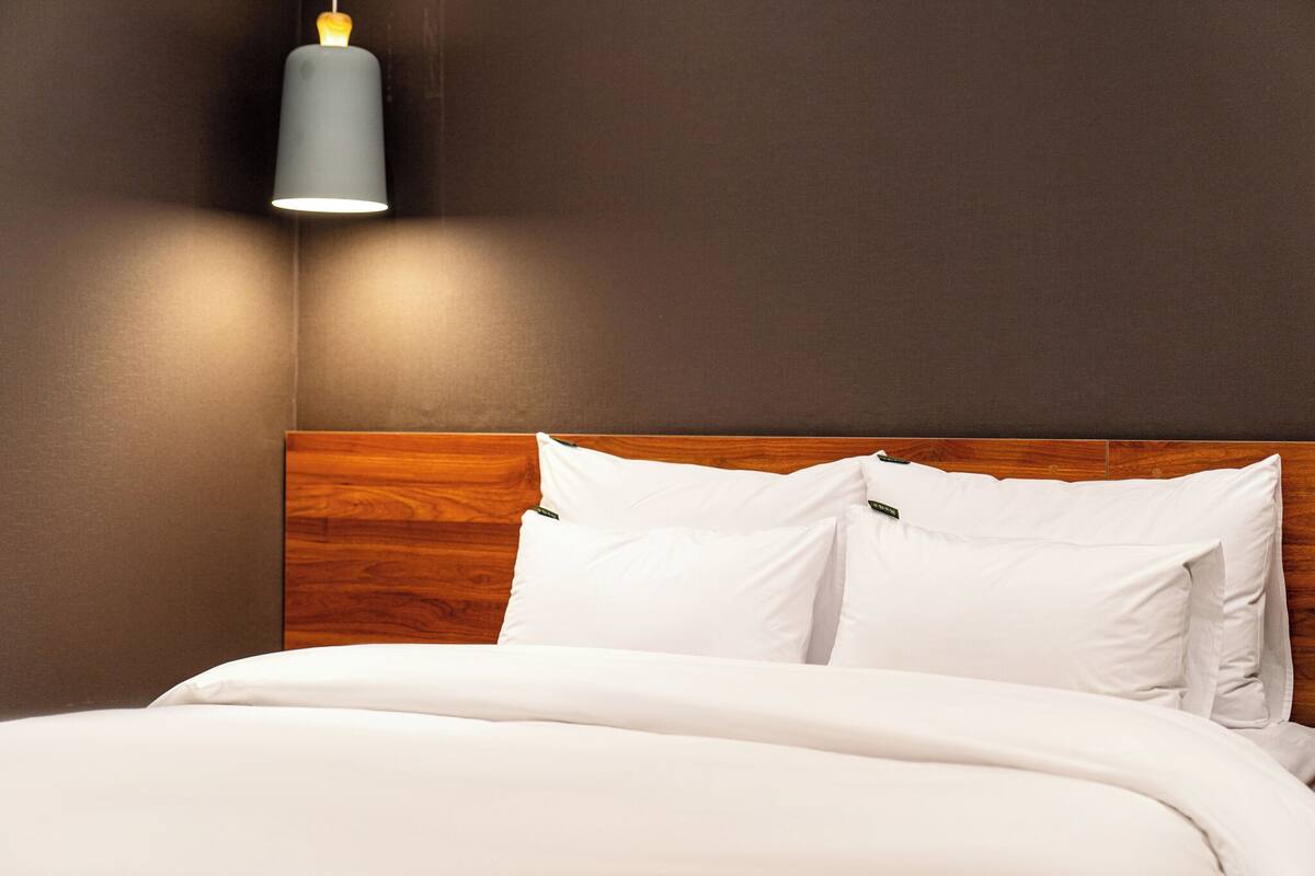 Een netjes opgemaakt bed met wit beddengoed en kussens, een houten hoofdbord en een modern wandlamp.