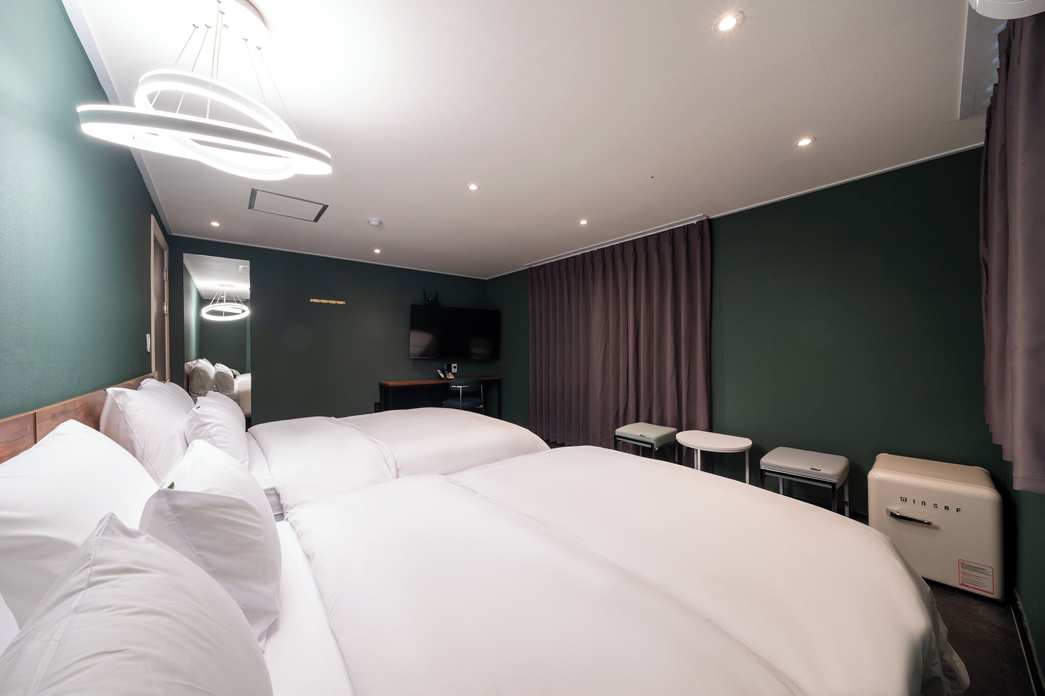A hotel room with two large beds, a small table, a chair, a TV, and a minibar.