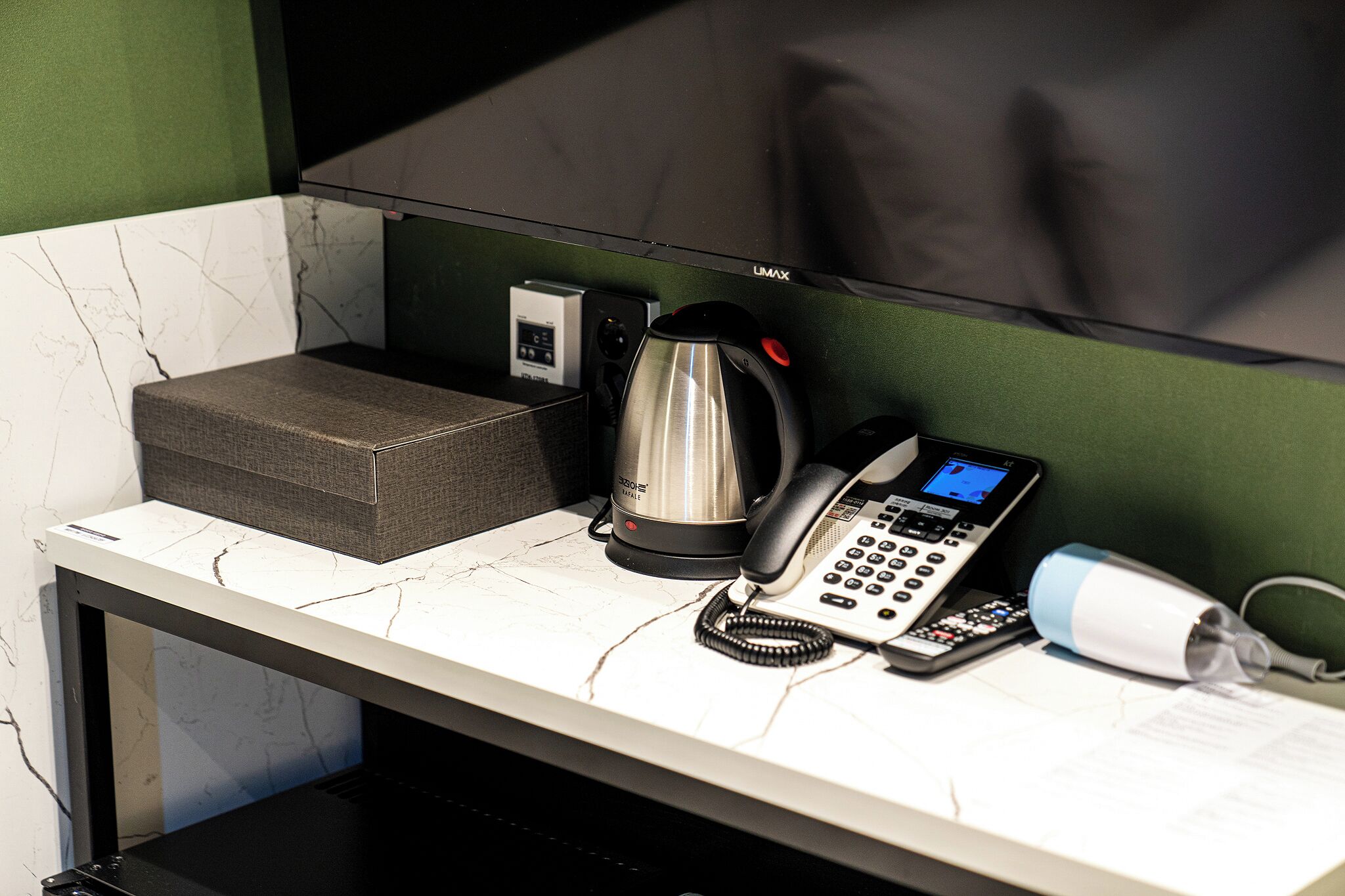 Escritorio de habitación de hotel con un teléfono, una tetera y una pequeña caja.