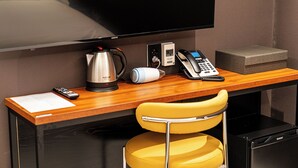 Habitación de hotel con un escritorio de madera, una silla amarilla, un televisor, una cafetera, un teléfono y una caja pequeña.