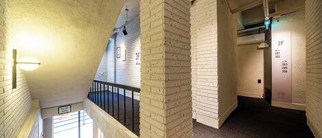 A corridor with white brick walls, a black railing, and a fire extinguisher.