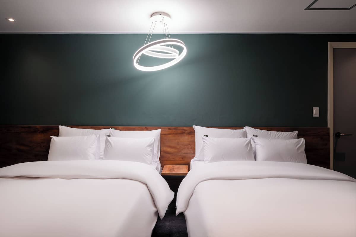 Een tweepersoonsbed met witte lakens, een houten hoofdbord en een modern, rond lichtarmatuur erboven.