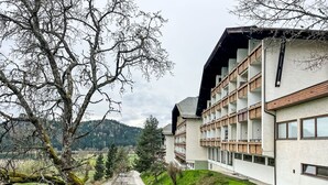 A modern building with multiple balconies, a paved pathway, and a view of a green landscape with trees and hills in the background. - Apartment Wolf by Interhome (Feldkirchen in Kärnten)