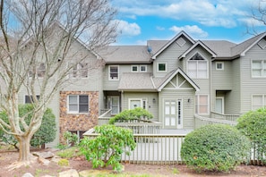 A two-story house with a stone accent wall, multiple windows, and a fenced yard with trees and shrubs.