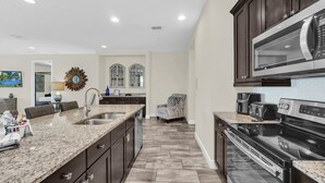 Una cocina moderna con encimeras de granito, armarios oscuros, una isla grande y un microondas integrado.