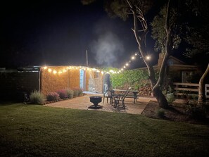 Un edificio de piedra con luces colgantes, una fogata y asientos al aire libre.