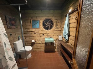 Un baño rústico con pared de piedra, inodoro, lavamanos y zona de ducha.