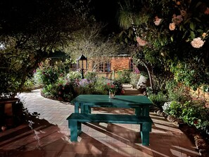 Un jardín con un banco de madera, un camino de ladrillo y un edificio con ventanas al fondo.
