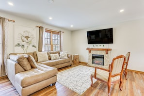 A living room with a beige sectional sofa, a wooden floor, a stone fireplace, and a flat-screen TV mounted above it.