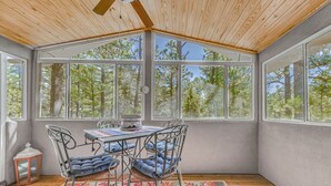 Une véranda avec un plafond en bois, de grandes fenêtres, une table avec des chaises et un tapis à motifs.