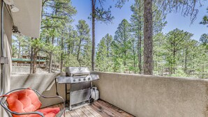Un balcon avec un barbecue, une chaise rembourrée rouge et une vue sur une zone boisée.