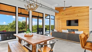 A modern interior with a wooden dining table, bench seating, a sofa, and a TV mounted on a wooden wall. - Outbound Ranch, Hot tub, Sauna, Fireplace, Views! (fredericksburg)