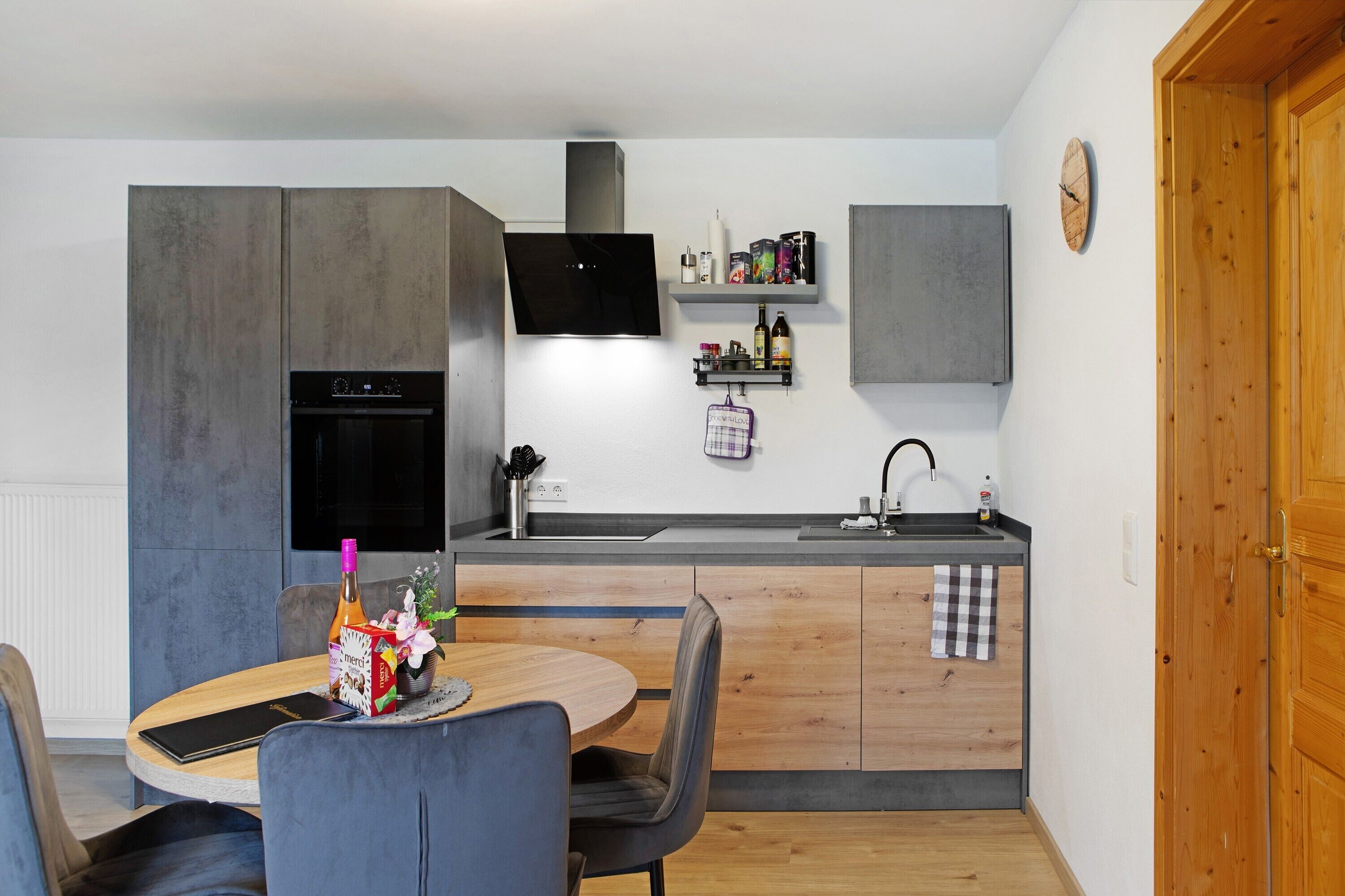 A compact kitchen with a built-in oven, a flat-screen TV, and a wooden dining area with a table and chairs.