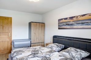 Een slaapkamer met een bed, een kledingkast, een nachtkastje en een schilderij van een zonsondergang boven de oceaan.