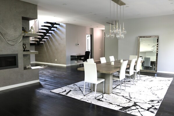 Un comedor moderno con una mesa grande y sillas, un tapete estampado y una escalera que conduce a un nivel superior.