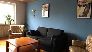 A living room with a sofa, armchair, wooden coffee table, and a wall-mounted lamp. - Apartment 'Business' with Sea View, Balcony and Wi-Fi (Weiden in der Oberpfalz)