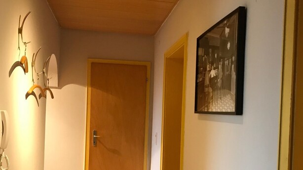 A hallway with a wooden door, a bench, a wall-mounted light fixture, and a framed picture. - Apartment 'Business' with Sea View, Balcony and Wi-Fi (Weiden in der Oberpfalz)