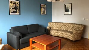 A living room with a dark grey sofa, a floral-patterned sofa, a wooden coffee table, and two framed pictures on the walls. - Apartment 'Business' with Sea View, Balcony and Wi-Fi (Weiden in der Oberpfalz)