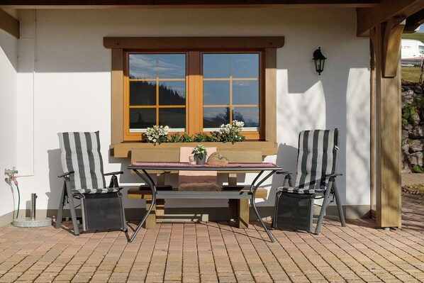 A patio with two striped chairs, a table, and a window with a view of a mountain.