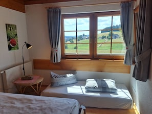 A bedroom with a bed, a window with curtains, a lamp, and a view of a green landscape.