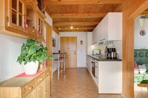 A kitchen with wooden cabinets, a dining area with stools, a potted plant, and a green upholstered bench.