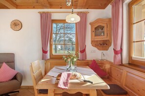 A wooden dining table with a loaf of bread, a knife, and a vase with flowers.
