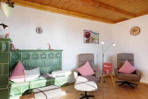 A room with a green cabinet, two armchairs with red and white checkered pillows, a small table with a red box, and a wall clock.