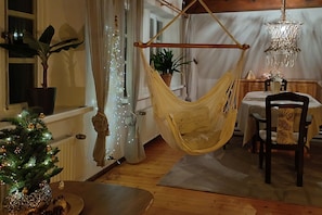 Une pièce chaleureuse avec un hamac, un sapin de Noël, une table à manger et un lustre.