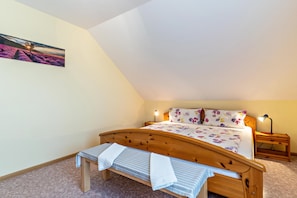 Un dormitorio con una cama de madera, un banco, una mesita de noche y una lámpara fijada a la pared.