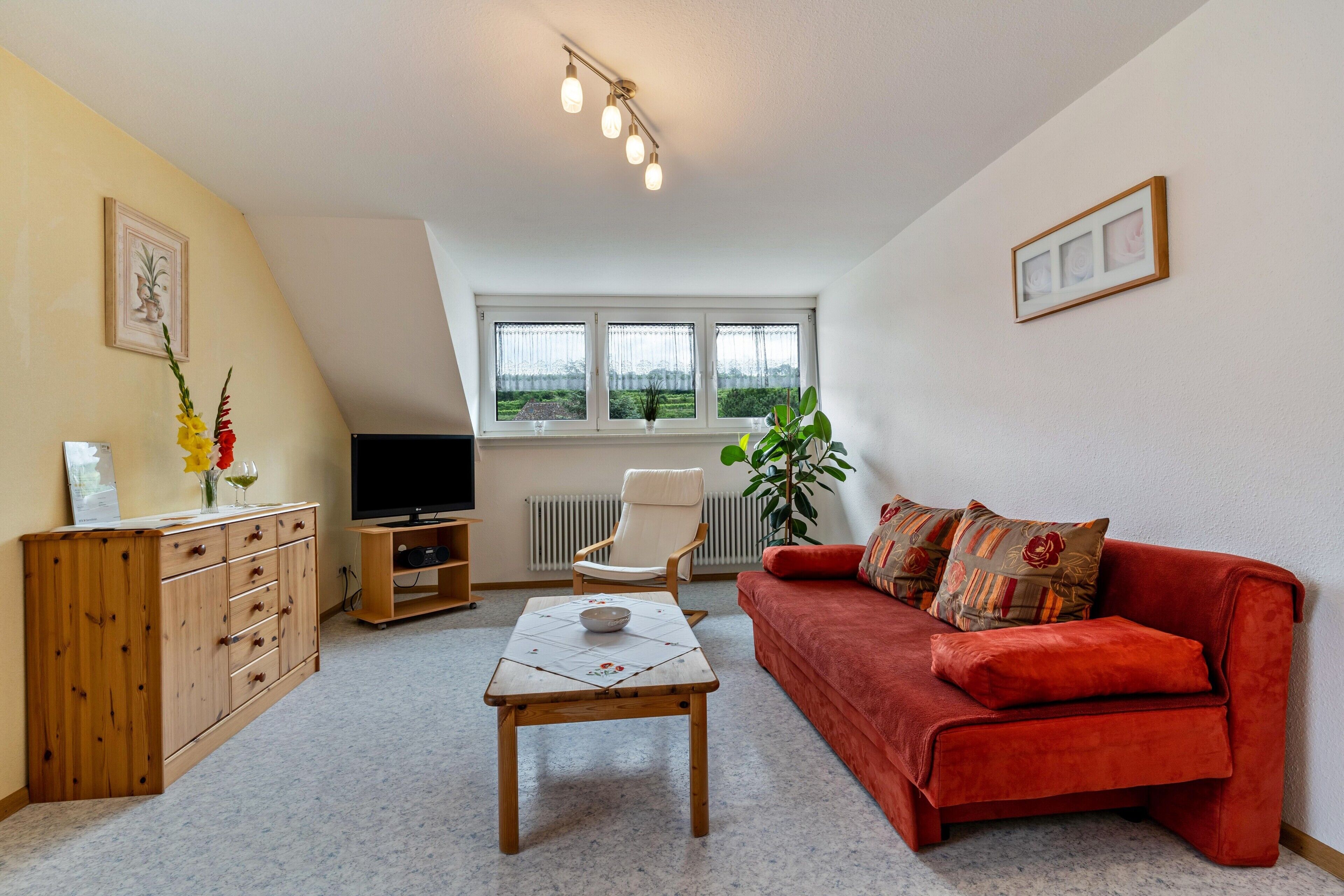 Ein Wohnzimmer mit rotem Sofa, Holzschrank, TV-Stand und einem Tisch mit einer Schüssel.