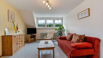 Ein Wohnzimmer mit rotem Sofa, Holzschrank, TV-Stand und einem Tisch mit einer Schüssel.