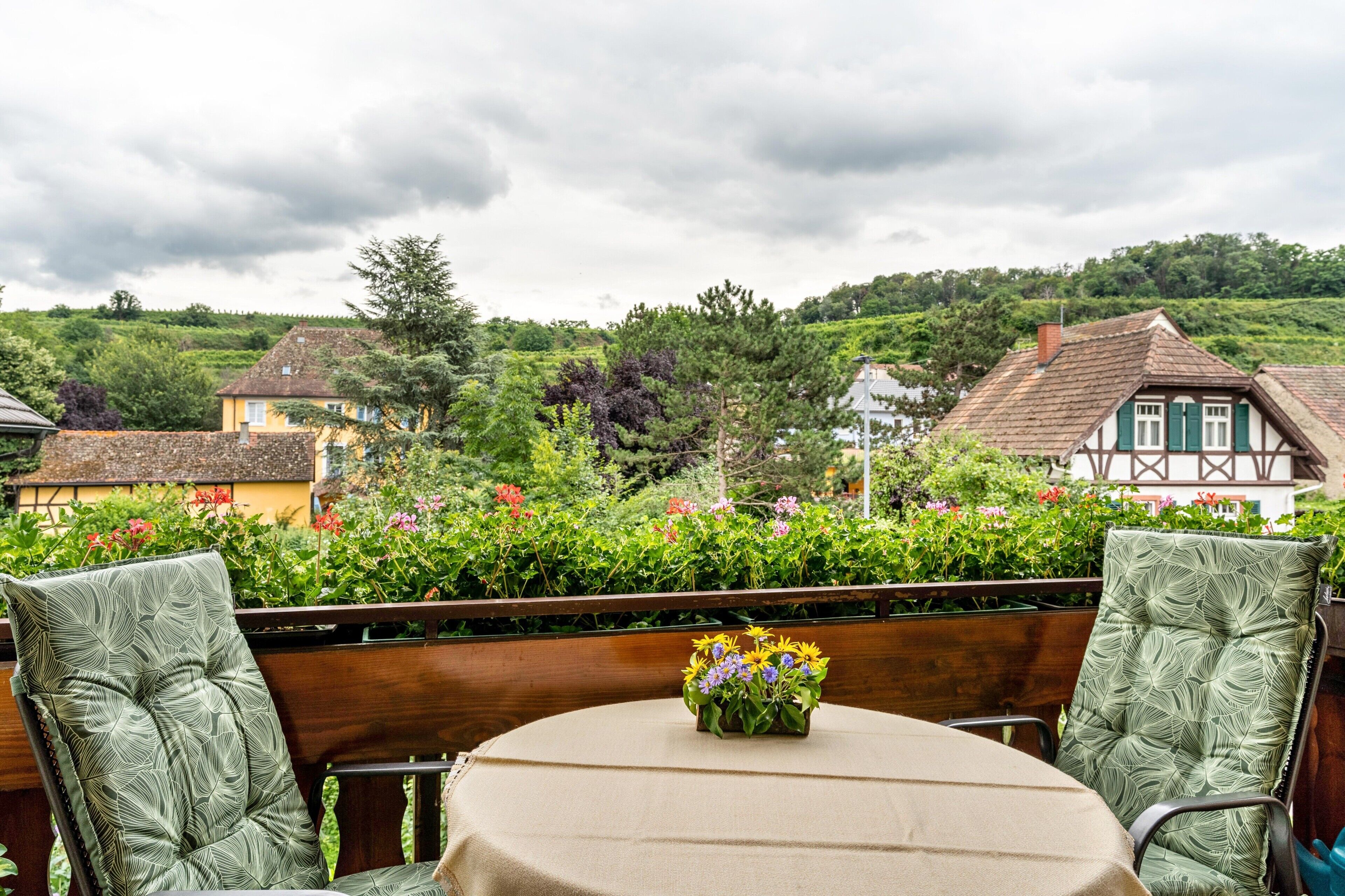 Eine Terrasse mit Tisch, Stühlen, einer Blumenvase und Blick auf Häuser und Grünflächen.