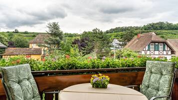 Eine Terrasse mit Tisch, Stühlen, einer Blumenvase und Blick auf Häuser und Grünflächen.
