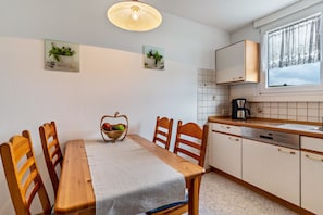 Una cocina con una mesa de madera, sillas, una cesta de fruta y una cafetera.