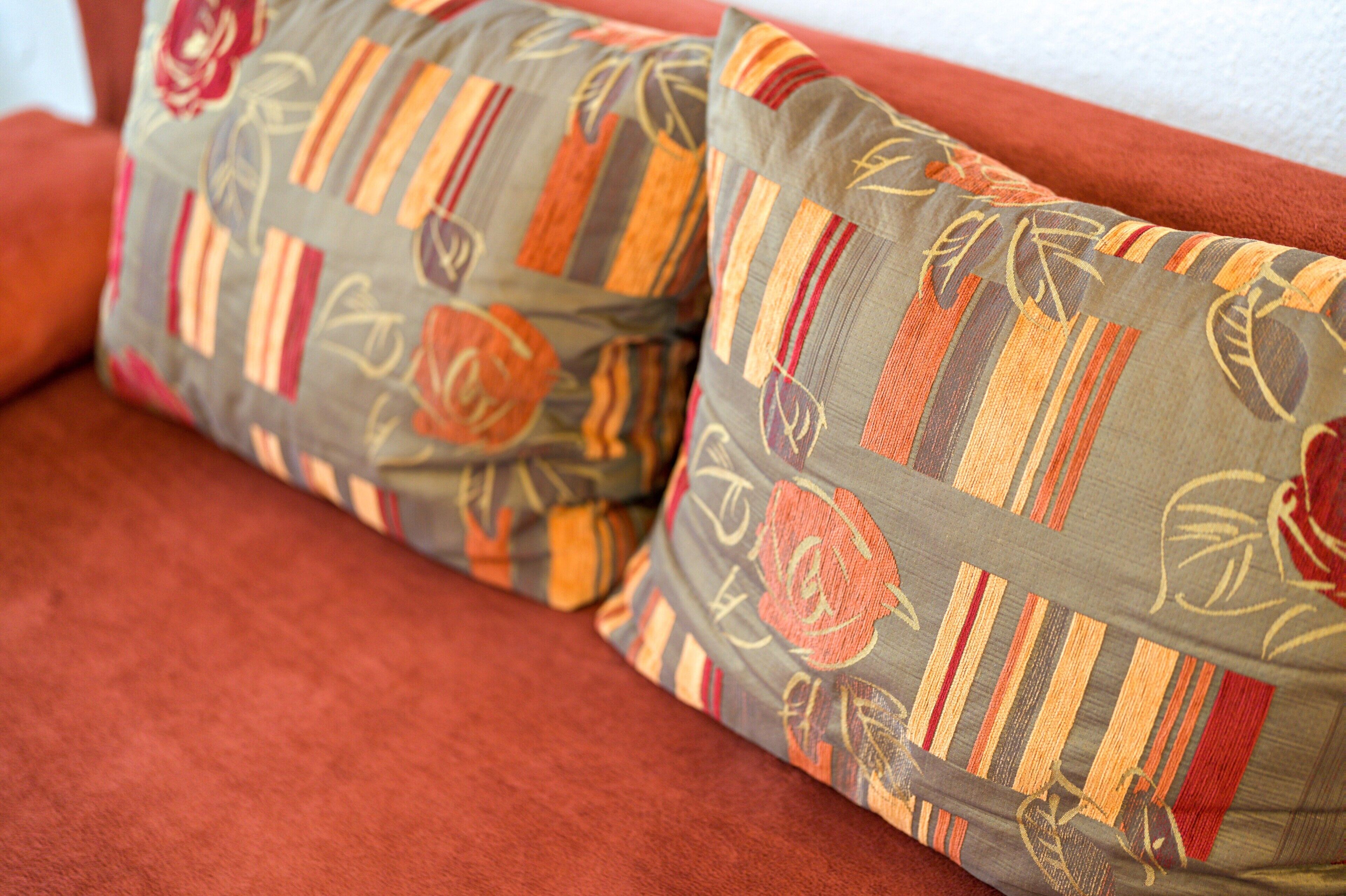Gros plan sur deux coussins à motifs posés sur un canapé rouge.