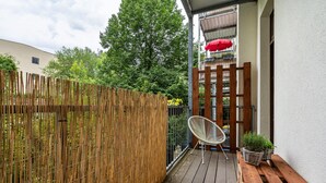Eine Holzterrasse mit Stuhl und Topfpflanzen, einem Bambuszaun und einem Gebäude mit Balkon.