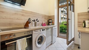 Eine kleine Küche mit Herd, Waschmaschine und einem großen Fenster.