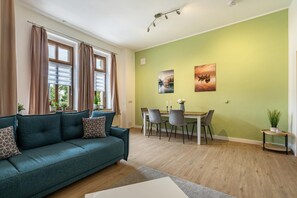 A living room with a sofa, dining table, chairs, and artwork on the wall.