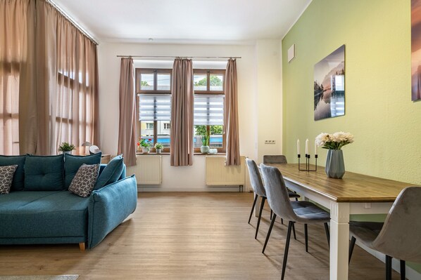 A living room with a sofa, dining table, chairs, and a view of a building outside.
