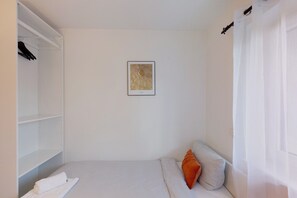 A bedroom with a bed, a white wall, a framed picture, and a closet.