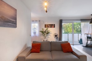 A modern living room with a sofa, a potted plant, a fan, and a dining area with a table and chairs.