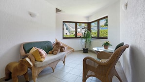 A corner room with a green sofa, wicker chairs, a small table with a plant, and a view of houses through a window. - Studio Apartment 'Pension Bergblick - Ringmauer' with Mountain View, Balcony and Wi-Fi (Marienberg)