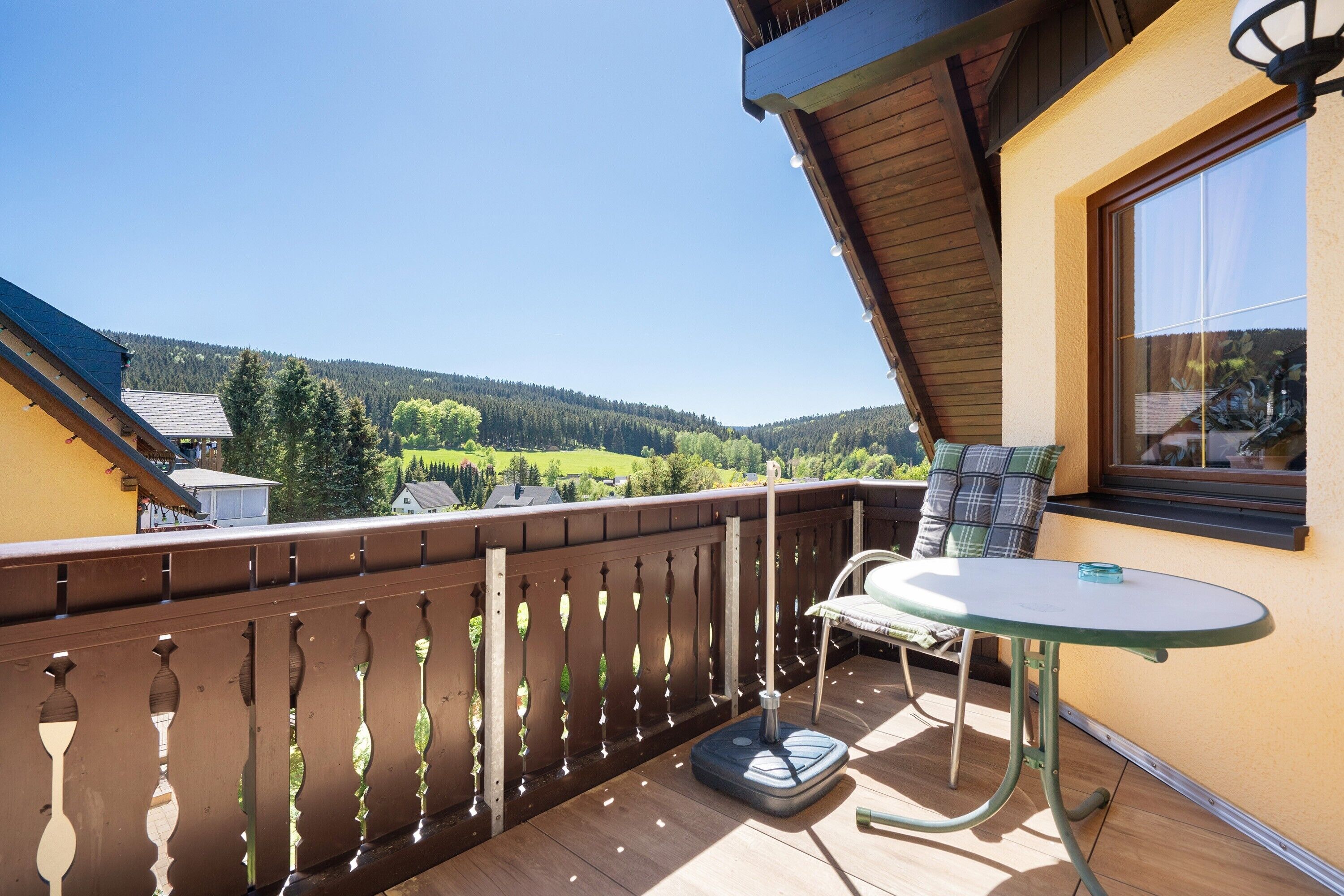 Ein Balkon mit Tisch und Stuhl, ein Fenster und Blick auf ein bewaldetes Gebiet.