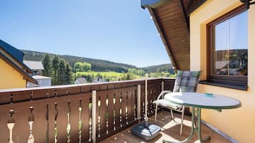 Ein Balkon mit Tisch und Stuhl, ein Fenster und Blick auf ein bewaldetes Gebiet.
