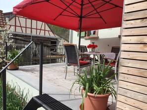 A patio with a red umbrella, outdoor seating, and potted plants.
